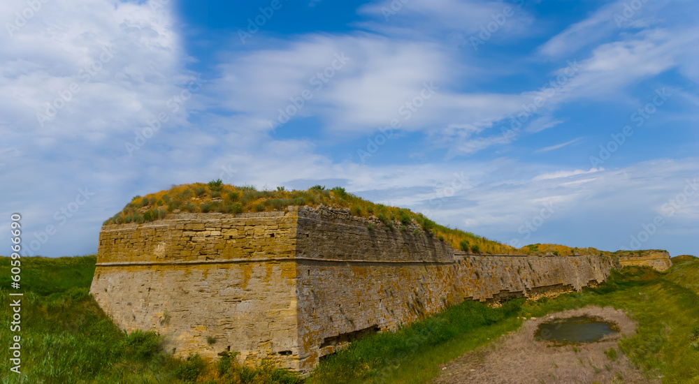 old medieval fortress wall among green fields under blue cloudy sky, open air museum scene