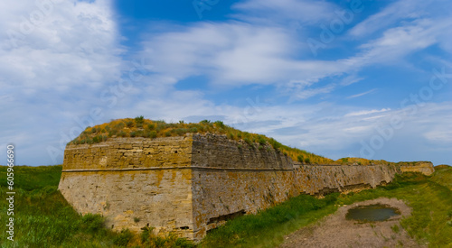 old medieval fortress wall among green fields under blue cloudy sky, open air museum scene