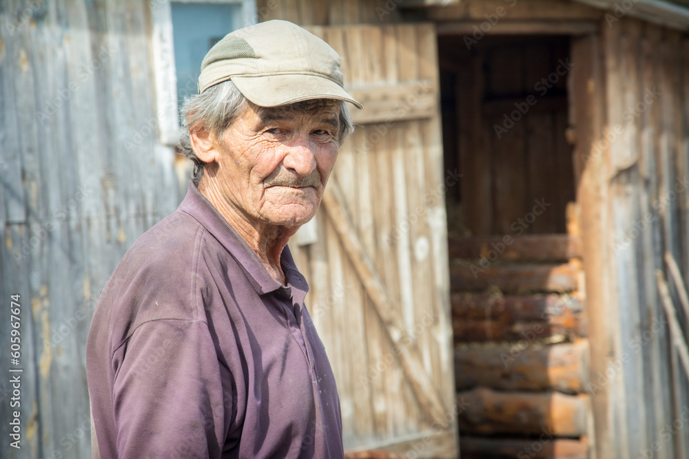 On a bright sunny day in summer, a portrait of an elderly man in a baseball cap and a short-sleeved shirt, standing in a rural yard. Village life. On a bright sunny day in summer, a portrait of an elderly man in a baseball cap and a short-sleeved shirt, standing in a rural yard. Village life.