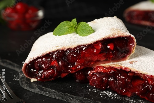 Delicious strudel with cherries, powdered sugar and mint on black table, closeup
