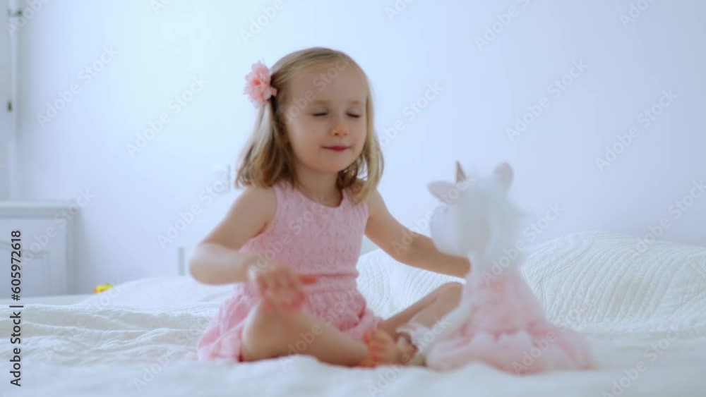 Adorable little girl in pink dress playing with unicorn. Kid having fun with soft toy. Child playing with stuffed toy