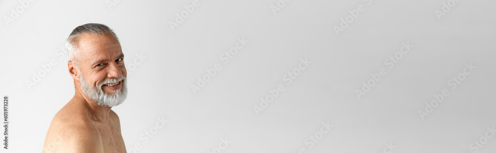 Portrait of handsome mature man with grey hair and beard, posing half-naked against grey background. Concept of male beauty, face and skin care, daily procedures, age. Banner. Copy space for ad Portrait of handsome mature man with grey hair and beard, posing half-naked against grey background. Concept of male beauty, face and skin care, daily procedures, age. Banner. Copy space for ad
