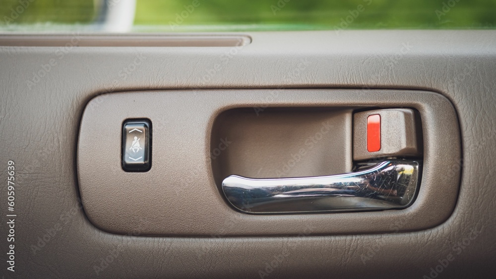 Closeup shot of the interior of a beige car's silver door handle with the lock