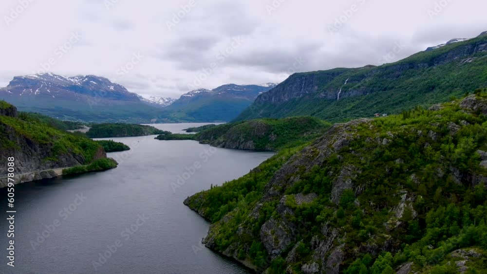 A calm Norwegian lake among forest-covered hills with snow-capped mountains in the background A calm Norwegian lake among forest-covered hills with snow-capped mountains in the background