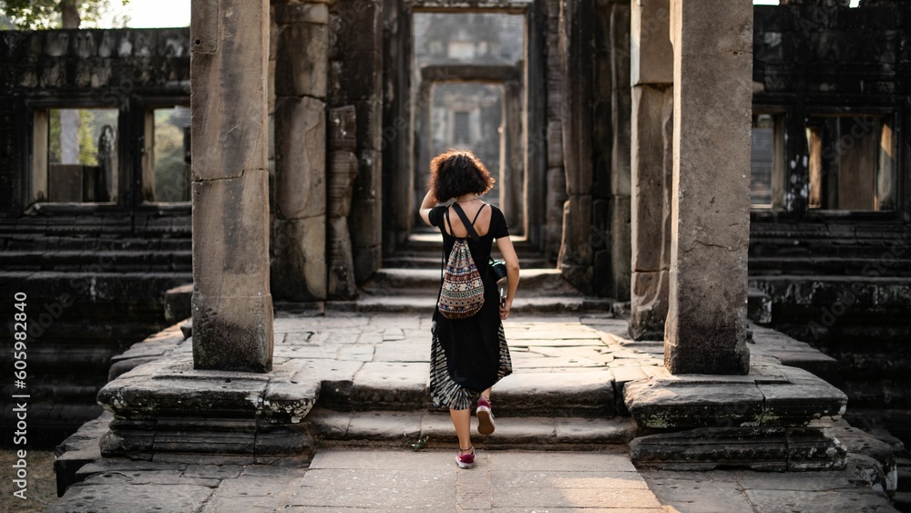 Back shot of a girl walking in a Temple in Siem Reap, Cambodia through stone columns Back shot of a girl walking in a Temple in Siem Reap, Cambodia through stone columns
