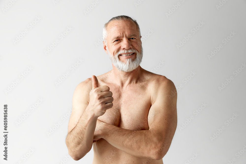 Fototapeta premium Portrait of handsome, mature, shirtless, muscular man with beard and gray hair posing against grey background. Positive attitude. Concept of male beauty, face and skin care, daily procedures, age