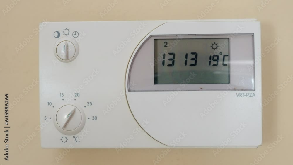 Close-up shot of a hand changing a mode of a thermostat showing the time and temperature of the room Close-up shot of a hand changing a mode of a thermostat showing the time and temperature of the room