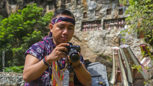 A young Asian man wearing a woven cloth is at Lemo which is a family burial site placed on a rock cliff photo