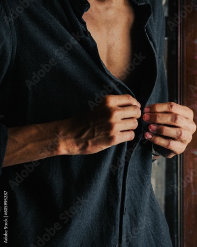 Vertical of a tanned fit man buttoning up his denim shirt with an exposed chest and veiny hands