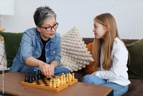 Little girl child plays chess with an adult grandmother at home on the table.
