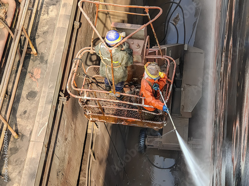 Shipyard labours are using hydroblast gun to remove marine growth on ship side
