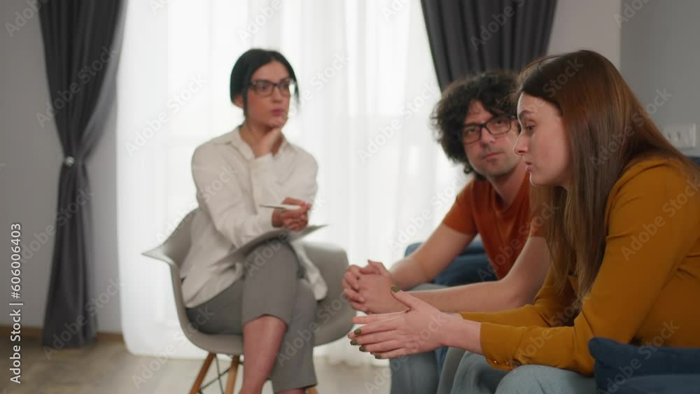 Couple having therapy session with a psychologist to solve their relationship problems and crisis. Sad man covering his ears with hands to avoid hearing abuse Couple having therapy session with a psychologist to solve their relationship problems and crisis. Sad man covering his ears with hands to avoid hearing abuse