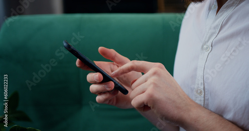 Close-up of the hands of unrecognizable young man typing smartphone and press the screen. Focused male holding smartphone and browsing internet sitting at home.