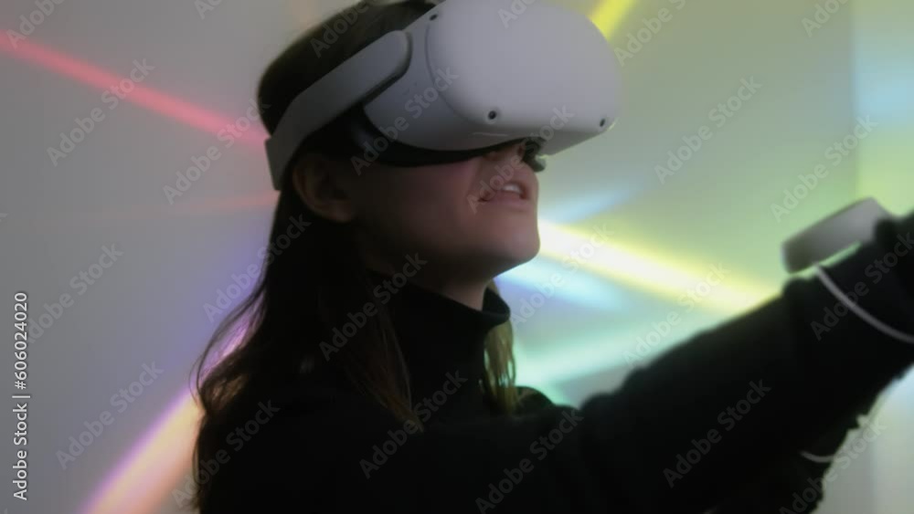 Young woman use virtual reality headset and joystick controllers for playing game or drawing. Female gamer or designer wearing vr goggles enjoys exploring 3D digital world and smiles Young woman use virtual reality headset and joystick controllers for playing game or drawing. Female gamer or designer wearing vr goggles enjoys exploring 3D digital world and smiles