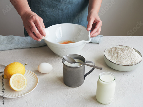woman's hands with egg on a bowl to mix ingredients and prepare a dessert or pastry recipe. Flour, milk and lemon on the table.