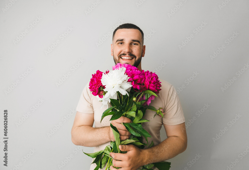 image of a handsome man with a bouquet of pink peonies as a gift. Smiling man with flowers, isolated on a gray background.