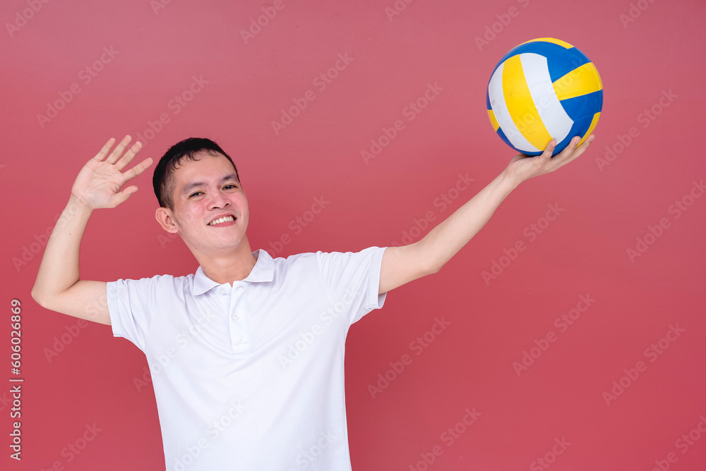 A sporty and athletic young man doing a volleyball serve position with the ball raised on one hand. Isolated on a red background.