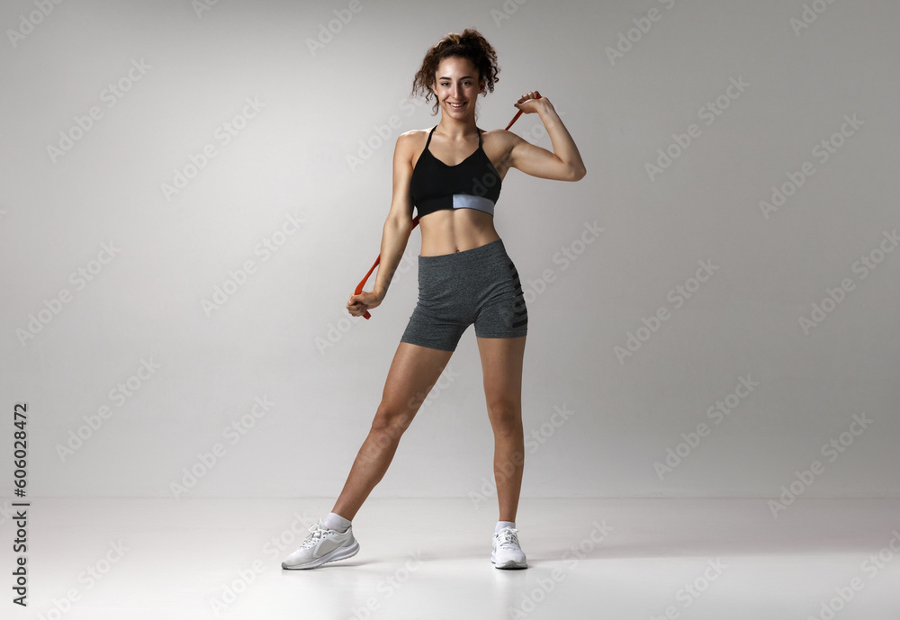Portrait of young girl in sportswear with musuclar body posing with fitness expanders against gray studio background. Concept of sportive lifestyle, beauty, body care, fitness, health Portrait of young girl in sportswear with musuclar body posing with fitness expanders against gray studio background. Concept of sportive lifestyle, beauty, body care, fitness, health