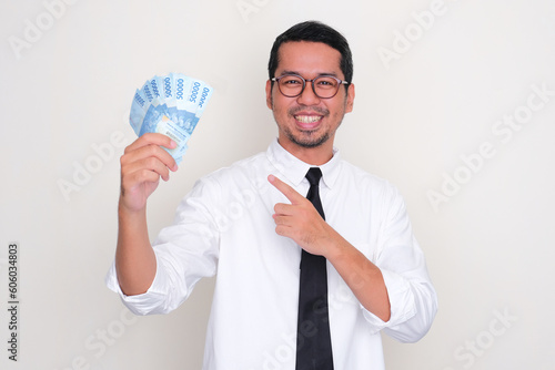 Adult Asian man smiling happy while pointing to the money that he hold photo