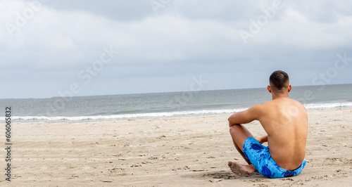 robust man without a shirt and shorts sitting in front of the beach