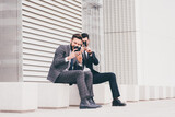 Two young contemporary businessman sitting using smart phone