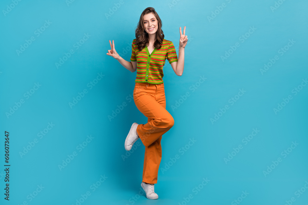 Full size photo of satisfied cheerful woman dressed orange pants colorful cardigan showing v-sign isolated on blue color background Full size photo of satisfied cheerful woman dressed orange pants colorful cardigan showing v-sign isolated on blue color background