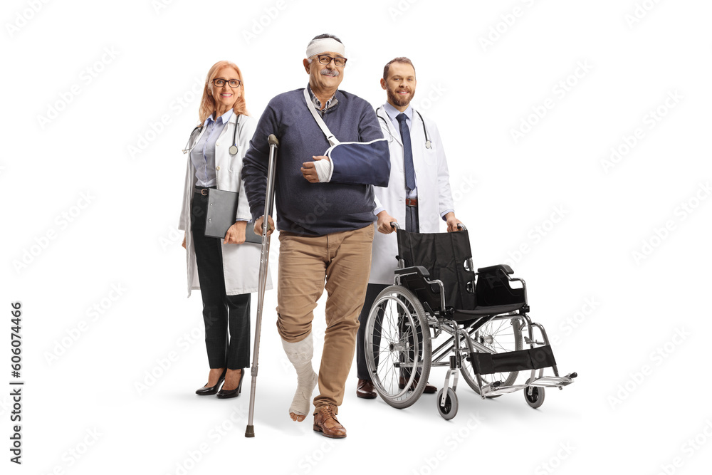 Doctors with a wheelchair standing behind a mature male patient with a broken leg and arm Doctors with a wheelchair standing behind a mature male patient with a broken leg and arm