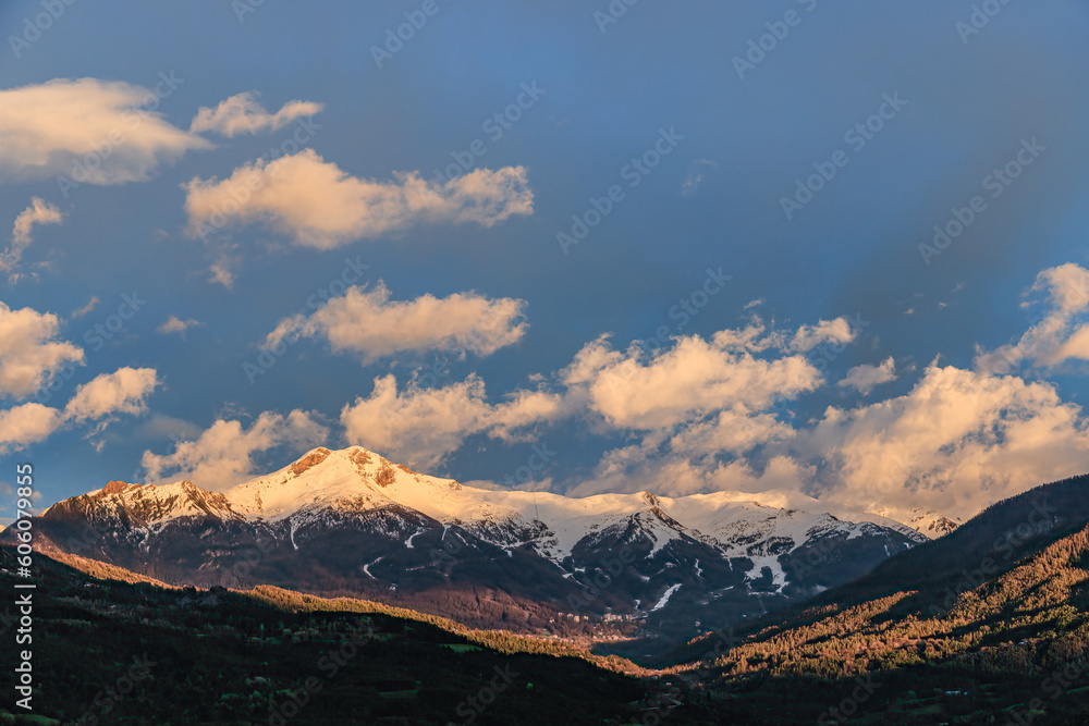 A scenics view of majestic snowy mountain summit (Les Orres) at golden hour, Hautes-alpes, France under a majestic blue sky and some white clouds