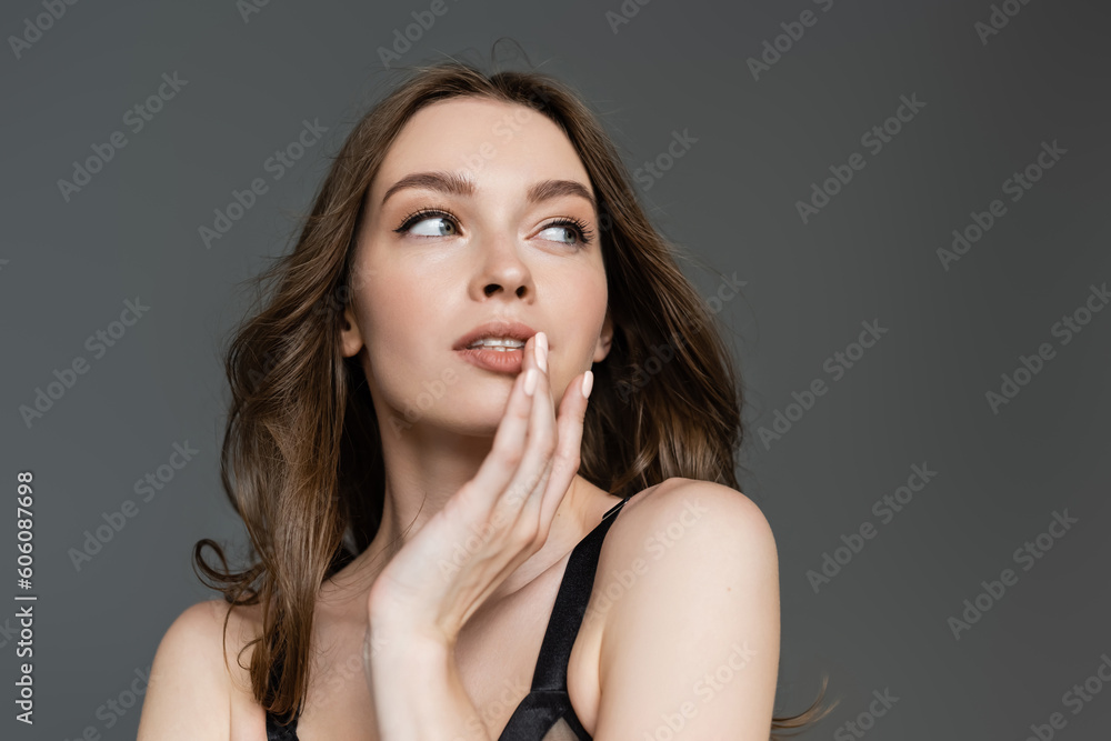 Portrait of seductive young brunette woman with natural makeup and modern hairstyle touching lips and looking away while posing isolated on grey, glamorous Portrait of seductive young brunette woman with natural makeup and modern hairstyle touching lips and looking away while posing isolated on grey, glamorous