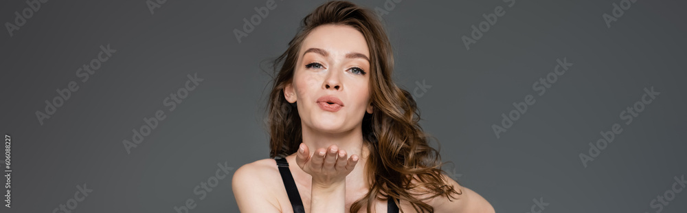 Pretty young model with natural makeup and brunette hair blowing air kiss while flirting and looking at camera while standing isolated on grey, banner Pretty young model with natural makeup and brunette hair blowing air kiss while flirting and looking at camera while standing isolated on grey, banner