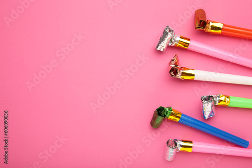 Party foil whistle or noise maker horn rolled on pink background.