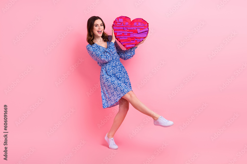 Full length photo of positive woman wear blue dress white shoes hands hold large heart present box isolated on pink color background Full length photo of positive woman wear blue dress white shoes hands hold large heart present box isolated on pink color background