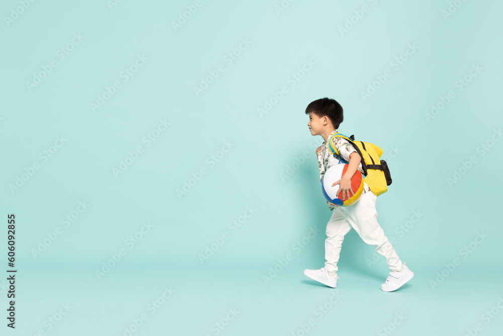 Asian little boy in flower pattern summer outfits holding beach ball and running with backpack isolated on green background, Five years old Asian little boy in flower pattern summer outfits holding beach ball and running with backpack isolated on green background, Five years old