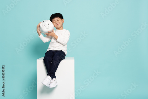 Fényképezés Portrait of happy Asian little boy holding white piggy bank isolated on green ba