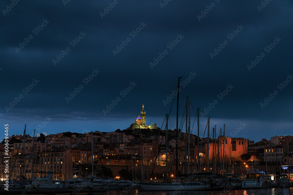 A scenics view of the city of Marseille, bouches-du-rhône, France at night with the old port in the with boats and the illuminated basilique notre-dame-de-la-garde (la bonne mère)