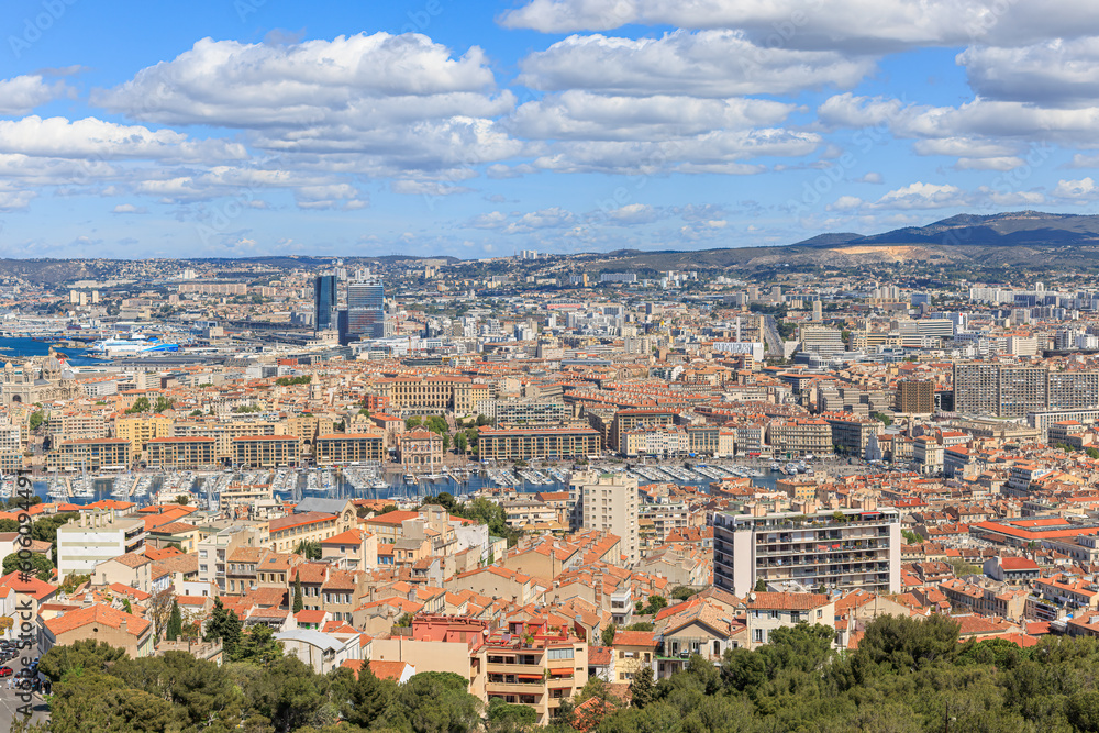 A scenics aerial view of the city of Marseille, bouches-du-rhône, France with the old port (vieux port) in the background under a majestic blue sky and some white clouds