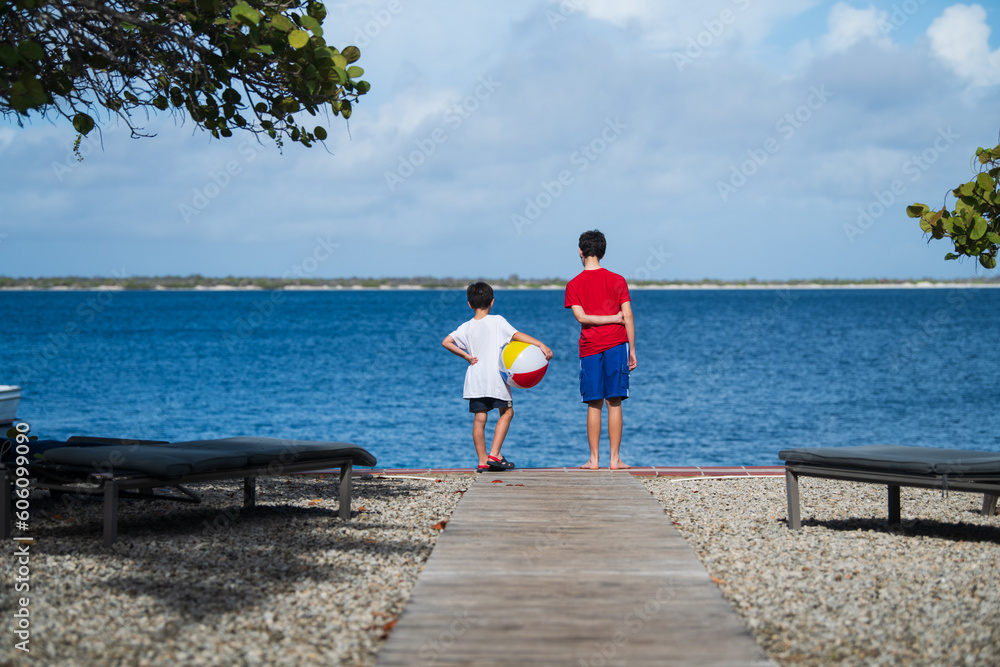 Two boys with a beach ball stand at the edge of a cliff overlooking the water in Bonaire, Leeward Antilles Two boys with a beach ball stand at the edge of a cliff overlooking the water in Bonaire, Leeward Antilles