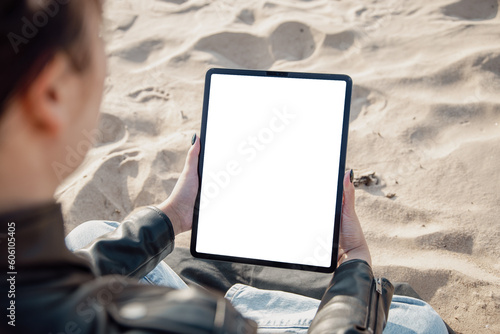 Women reading news or e-book on digital tablet similar to IPad while sitting by the sea in beach sand