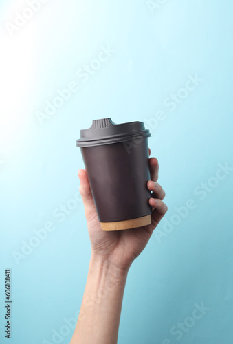 Hand holding brown Disposable take out cup for hot drinks (tea, coffee) on blue background