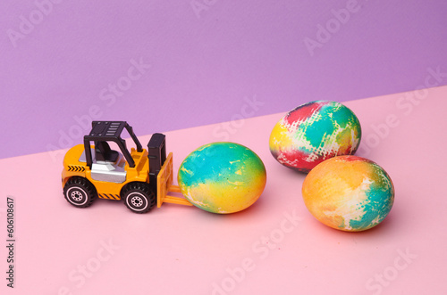 Toy forklift with Easter colored eggs on pastel color background. Minimalism Easter still life