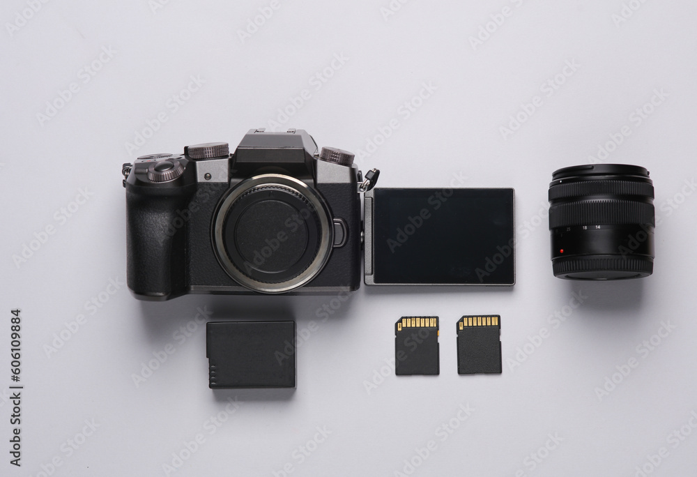 Modern digital camera with flip screen, two sd memory cards, battery and lens on gray background. Photographer's equipment. Top view. Flat lay