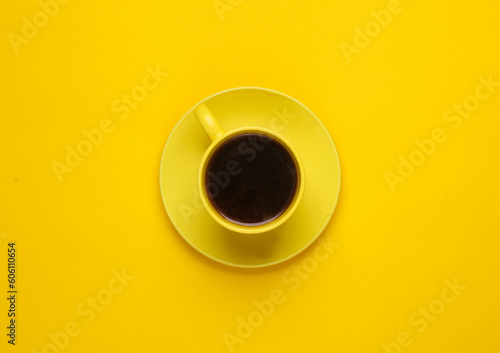 Yellow ceramic cup with coffee on a saucer, yellow background. Top view