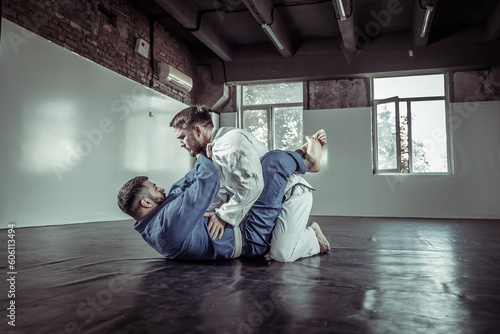 Two fighters sparring a partner in a kimono are training painful holds in a sports hall photo
