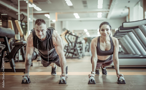 Fototapeta Naklejka Na Ścianę i Meble -  Workout together. Athletic man and woman are training doing push-ups in the gym. Healthy lifestyle