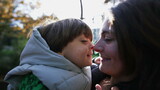 Happy mother and child doing eskimo kiss with nose standing outdoors with sunlight flare. Motherhood lifestyle concept