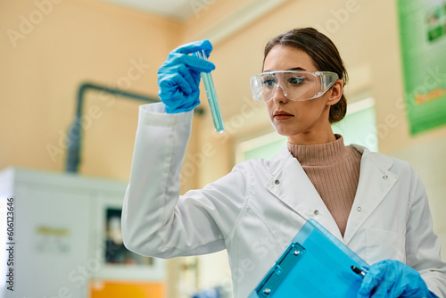 Young female biochemist examining liquid in test tube while working in lab.