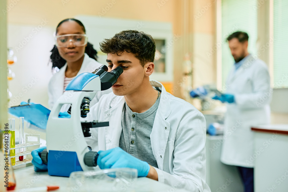 Young biochemist looking through microscope during research in lab. Young biochemist looking through microscope during research in lab.