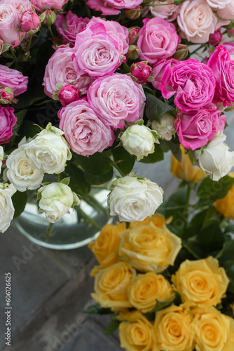 Flowers in a glass vase on the steps of a flower shop. Fresh peony and yellow roses outside. Master classes and floristry courses. Flower delivery.