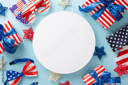Festive setup for American Independence Day. From above, you can see top view party decor including rattan stars, necktie, bow-tie, eyeglasses, gift boxes, on a blue backdrop with space for text or ad