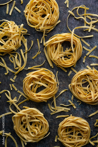 Tagliatelle Pasta Nests Surrounded by Scattered Broken Noodles: Several dried pasta nests of noodles placed on a kitchen countertop